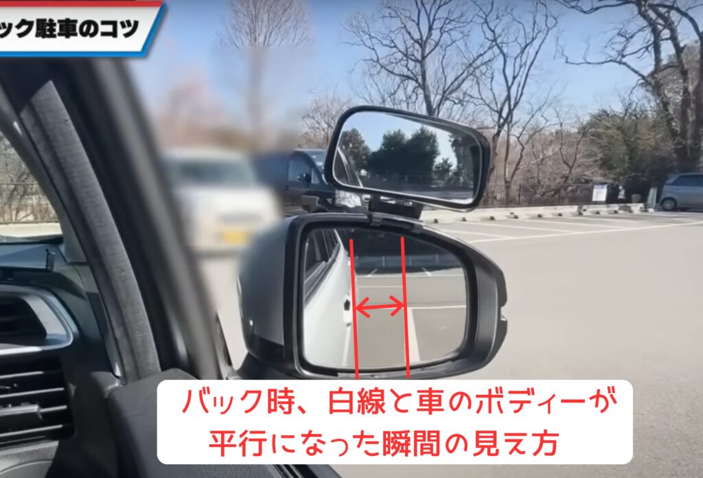 バック駐車ステップ6の解説図。サイドミラーに映る白線と車のボディが平行になった瞬間が、停止の目安となることを示している。このタイミングで一旦停止し、ハンドルをまっすぐ正面に戻してから再びバックすることで、駐車位置が安定し正確に枠内へ収まる。